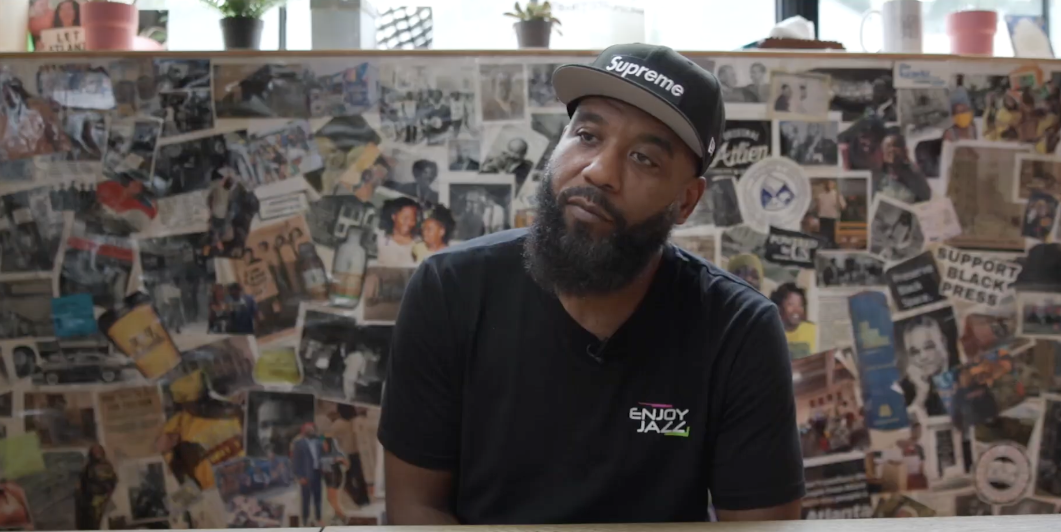 Portrait of Brian Page seated during an oral history interview in front of a collage of historic photographs and community images.